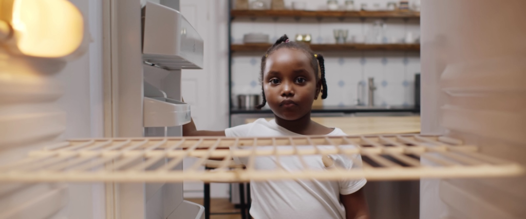 hungry poor little african girl look for food in empty fridge at home.